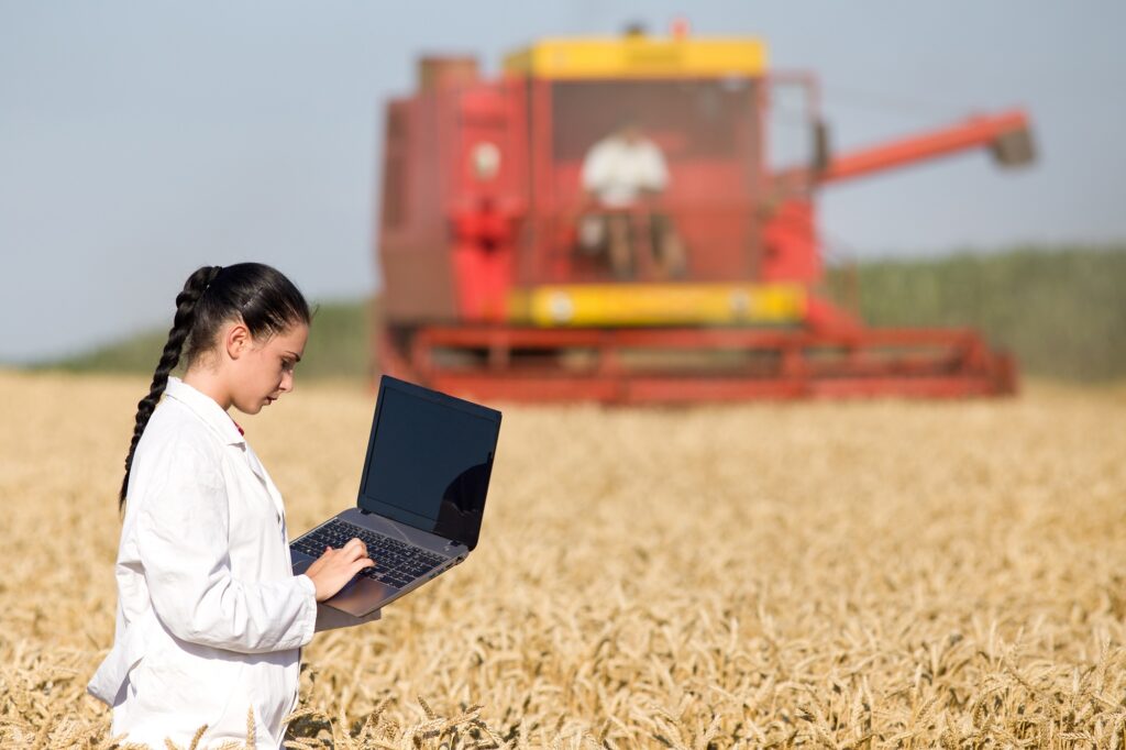 junge Frau mit Laptop auf einem Feld mit Mähdrescher